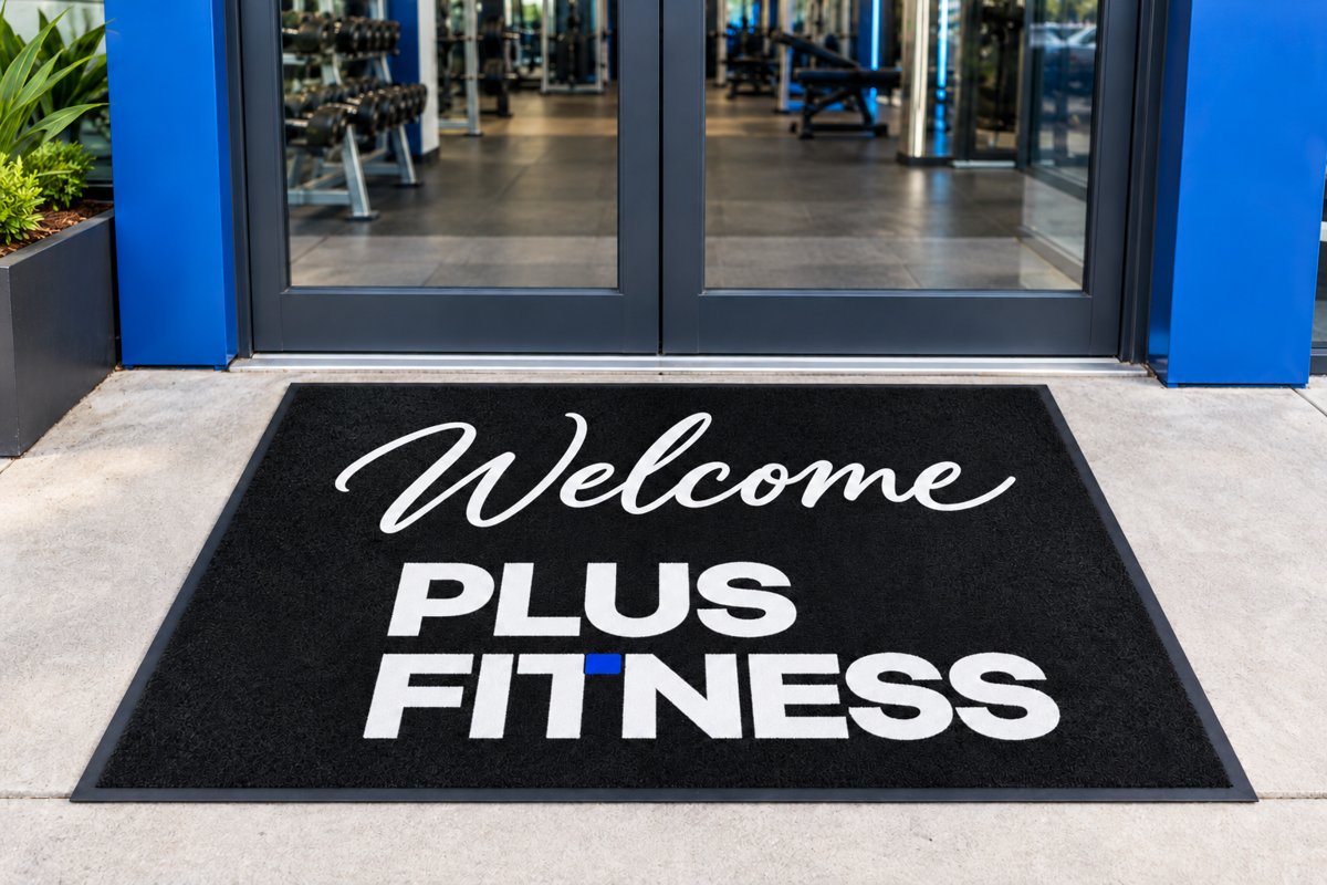 Welcome Plus Fitness logo mat at a gym entrance